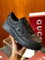 Sneaker luxury Gucci in pelle nera con logo embossato e suola leggermente rialzata.