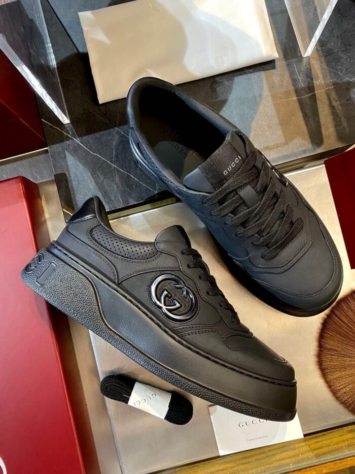 Sneakers nere di lusso con emblema elegante su superficie riflettente, stile moderno e sofisticato.