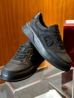 Scarpe sportive nere in pelle con logo embossato, stile elegante e moderno, su superficie in vetro.
