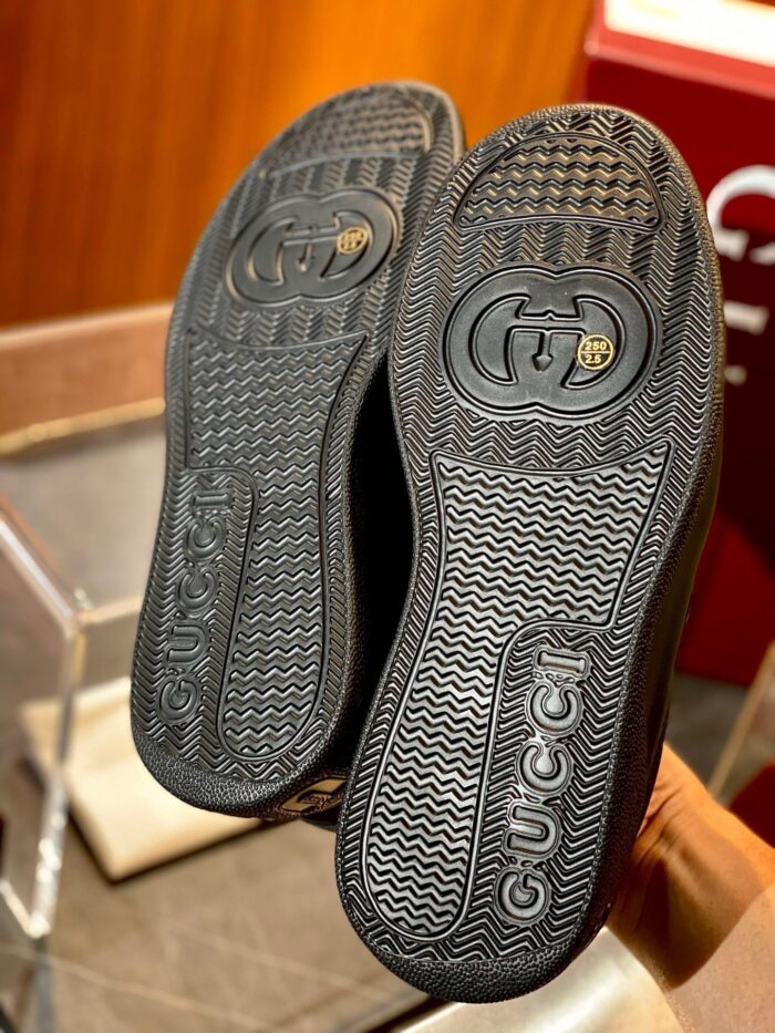 Sneakers di lusso nere con suola dettagliata e logo elegante in ambiente raffinato.