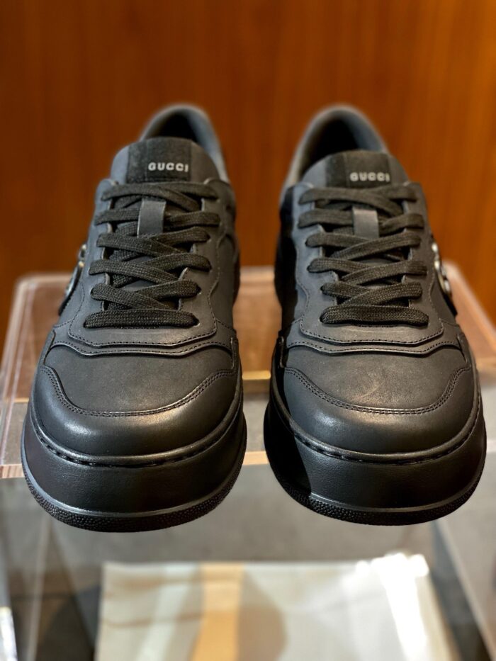 Sneakers nere in pelle elegante, design minimalista, su sfondo in legno raffinato.