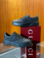 Sneakers Gucci nere minimaliste su sfondo di legno con scatola rossa elegante.