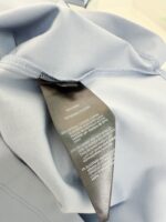 Maglietta blu leggero con etichetta di cura e cuciture precise, stile minimalista e versatile.