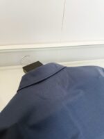 Camicia blu elegante con dettagli di ricamo sul colletto, su appendiabiti nero, sfondo bianco semplice.