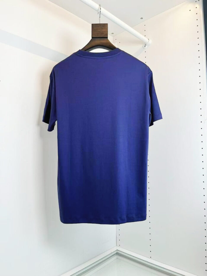 Maglietta viola dal taglio classico, morbida e versatile, su appendiabiti in ambiente minimalista.