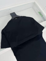 Maglietta nera minimalista su appendiabiti in ambiente moderno e luminoso.
