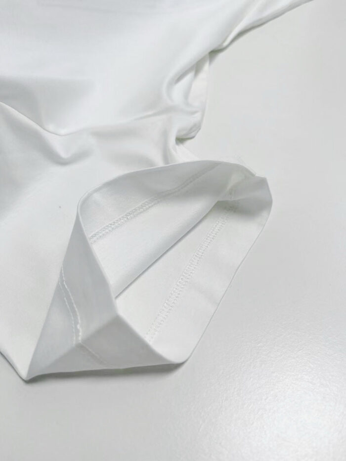 Cucitura elegante su manica di cotone bianco, dettagli raffinati e finitura curata.