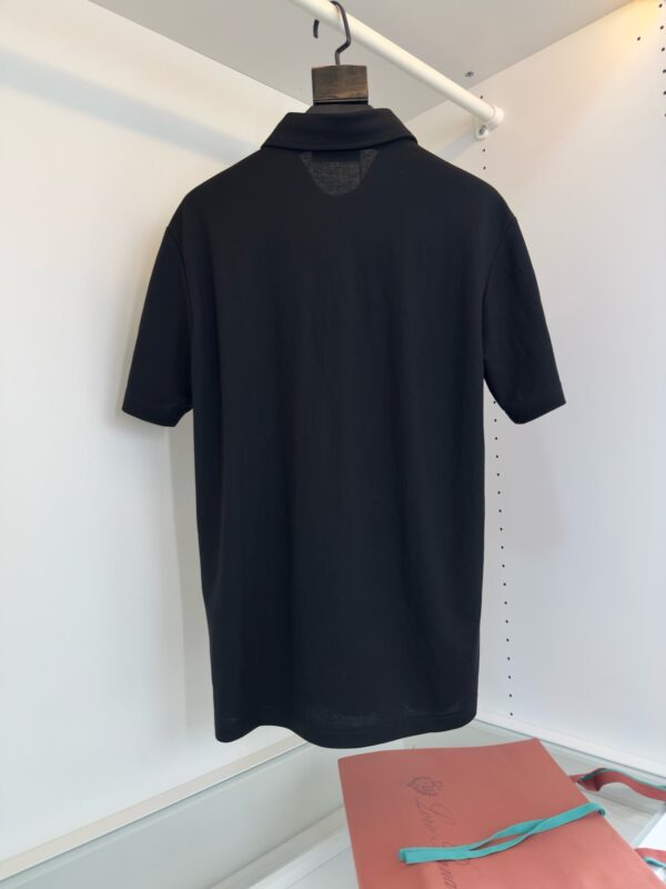 Maglietta polo nera elegante su appendino in ambiente minimalista, ideale per look casual e raffinati.