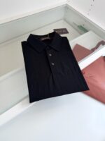 Maglietta polo nera elegante su superficie in vetro con accessori e branding visibile.