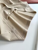 Tessuto in cotone beige, morbido e elegante, ideale per abbigliamento casual e comodo.