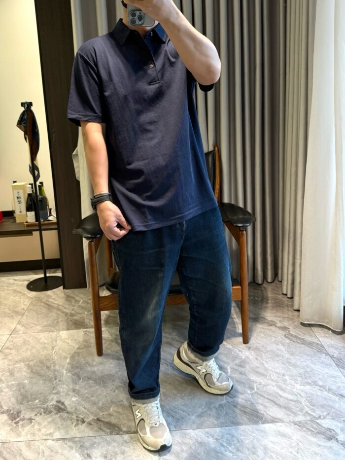 Uomo in outfit casual con polo navy, jeans e sneakers chunky, in ambiente domestico elegante.