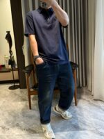 Persona con polo navy, jeans distressed e sneakers bianche in ambiente domestico casual.