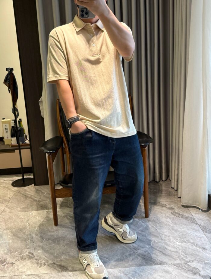Look casual elegante con polo beige, jeans scuri e sneakers trendy in ambiente moderno.
