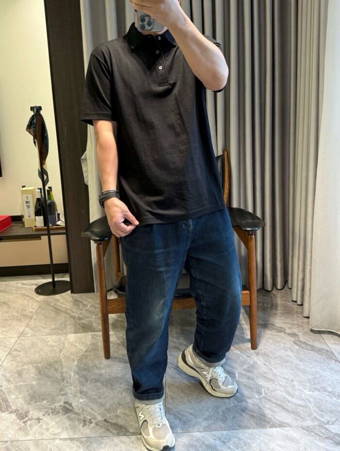 Persona con polo nero, jeans blu e sneakers in ambientazione casalinga luminosa.