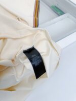 Maglietta beige con etichetta nera minimalista, stile moderno e elegante, su sfondo neutro.