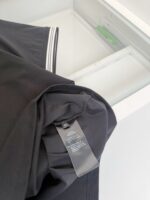 Camicia nera con etichetta, dettagli eleganti e ambiente ordinato in sfondo.