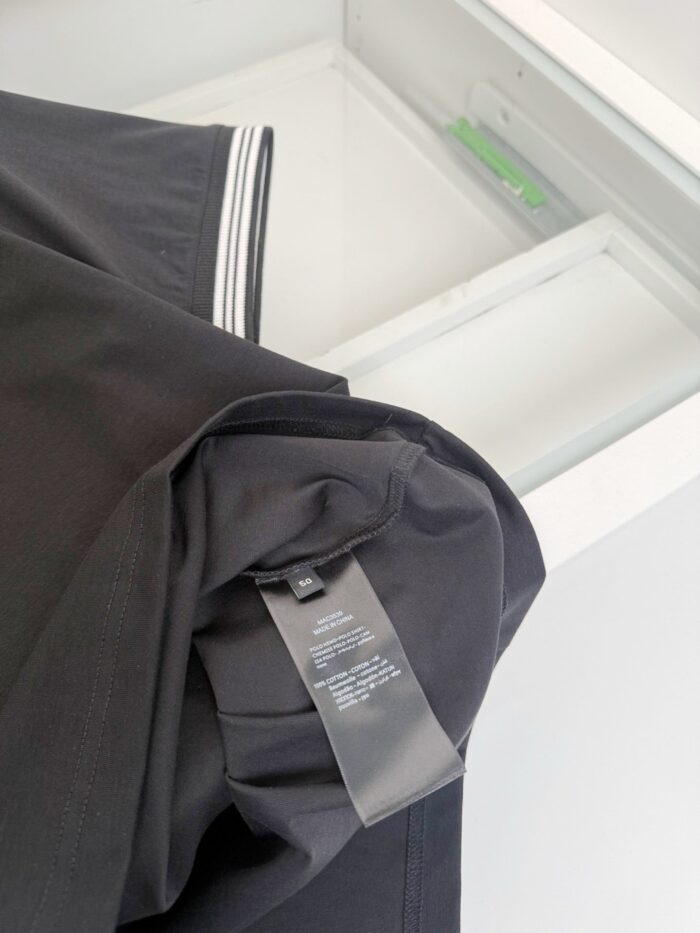 Camicia nera con etichetta, dettagli eleganti e ambiente ordinato in sfondo.