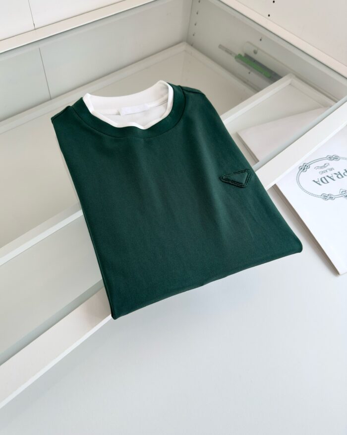 Maglietta verde scuro piegata con logo nero, stile casual e moderno su superficie chiara.
