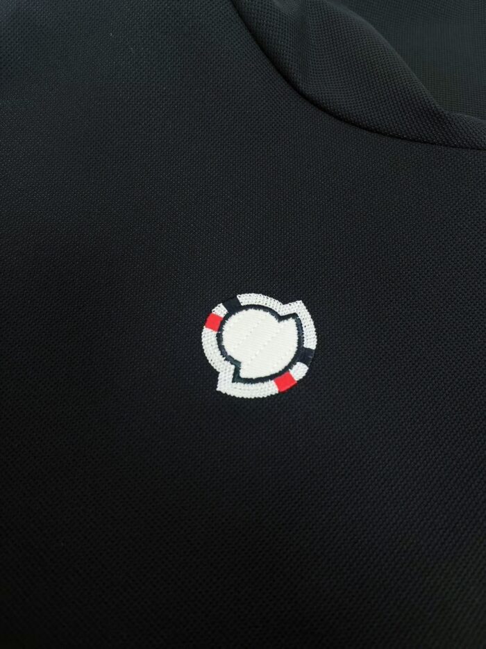 Logo minimalista con cerchio bianco e dettagli rossi su tessuto nero elegante.
