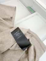 Blusa beige con etichetta moderna in ambiente ordinato e luminoso.