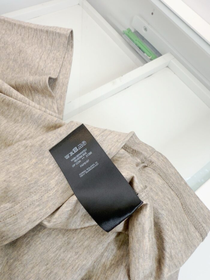 Blusa beige con etichetta moderna in ambiente ordinato e luminoso.