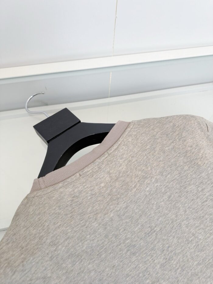 Maglietta beige su appendiabiti nero in ambiente minimalista e moderno.