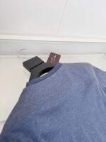Maglietta blu casual su gancio nero con etichetta elegante, ideale per look quotidiani.