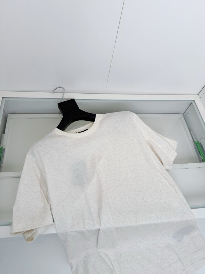Maglietta bianca casual su appendiabiti in ambiente minimalista e luminoso.