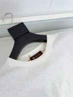 Maglietta bianca in cotone su appendino nero, stile minimalista e elegante.