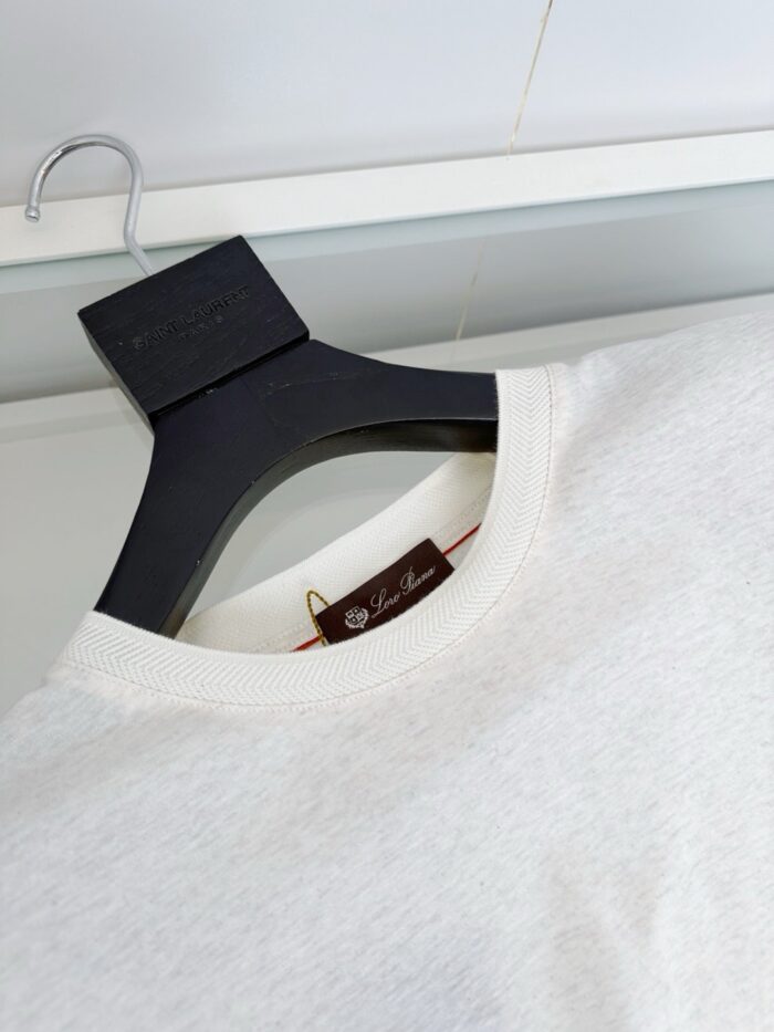 Maglietta bianca in cotone su appendino nero, stile minimalista e elegante.