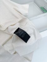 Tessuto leggero beige con etichetta di cura, ideale per abbigliamento casual e confortevole.