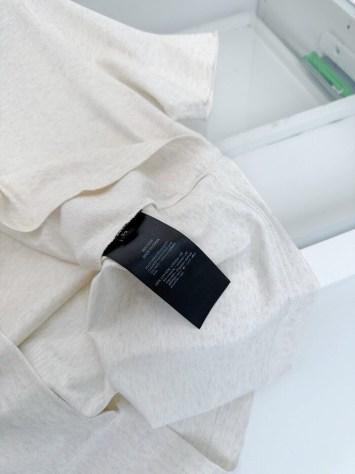 Tessuto leggero beige con etichetta di cura, ideale per abbigliamento casual e confortevole.