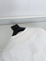 Maglietta bianca minimalista su gancio nero in sfondo neutro, stile moderno ed elegante.