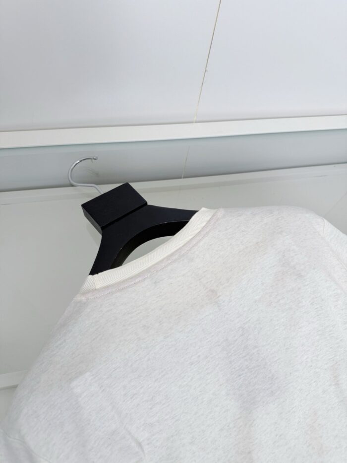 Maglietta bianca minimalista su gancio nero in sfondo neutro, stile moderno ed elegante.