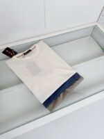 T-shirt grigia casual con dettagli colorati, su superficie in vetro, stile moderno e versatile.