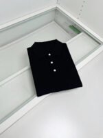 Maglietta polo nera elegante su superficie di vetro, stile minimalista e di alta qualità.