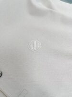 Tessuto bianco con logo ricamato moderno, finiture eleganti e dettaglio minimalista.