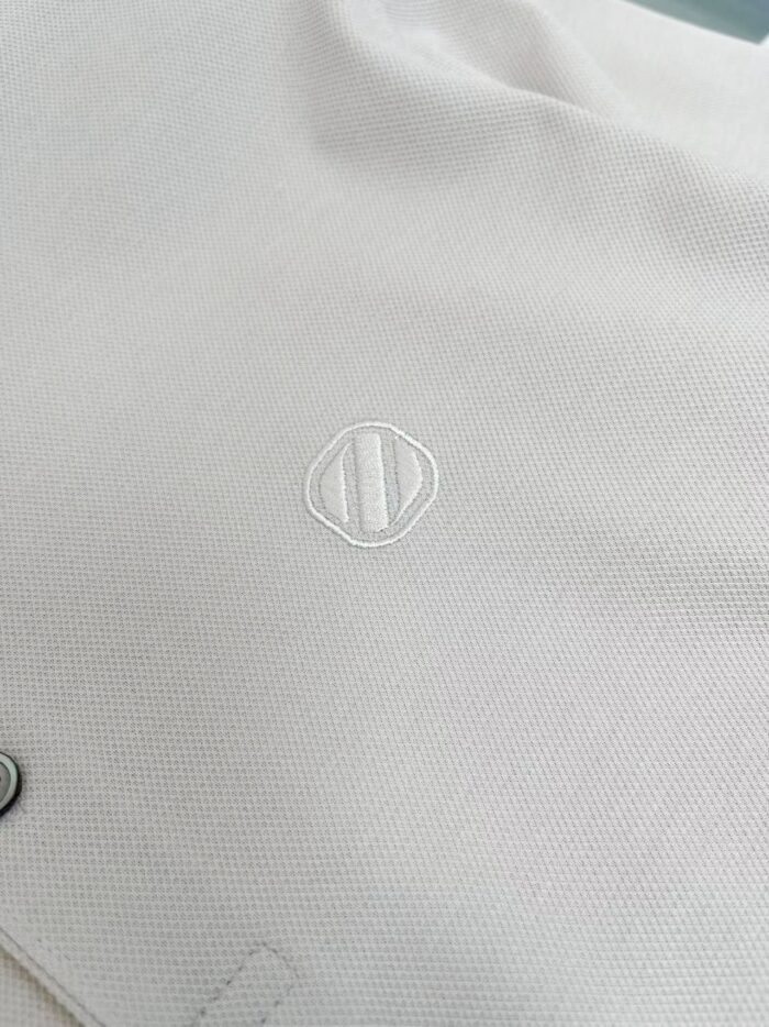 Tessuto bianco con logo ricamato moderno, finiture eleganti e dettaglio minimalista.