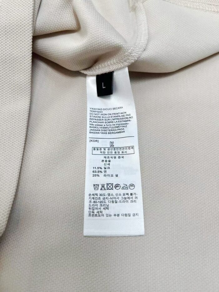 Etichetta di cura su maglietta beige, taglia L, con simboli e istruzioni di lavaggio.