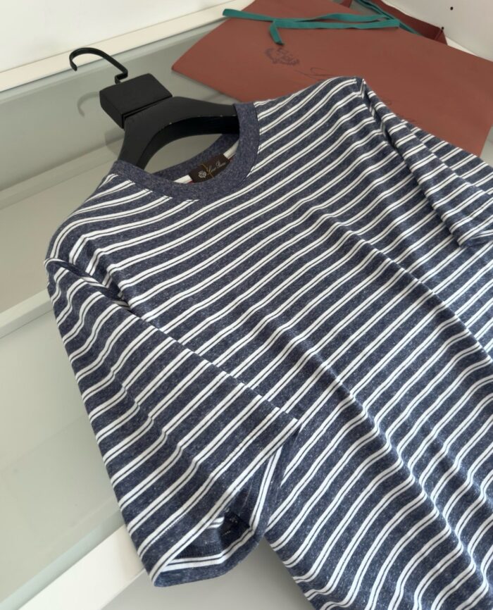 Maglietta a righe blu casual, con colletto scuro, su sfondo di tessuti colorati.
