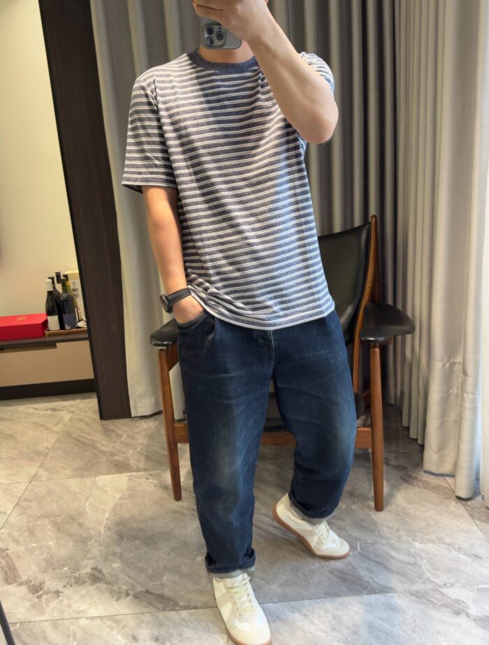 Giovane uomo in t-shirt a righe e jeans larghi con sneakers bianche, ambiente domestico luminoso.
