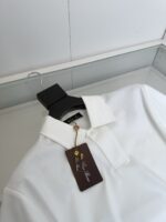 Maglietta polo bianca elegante su appendiabiti nero, stile versatile e di alta qualità.