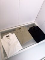 Set di polo classiche in bianco, verde oliva e blu navy su superficie in vetro.