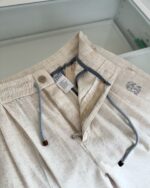 Pantaloni casual beige con elastico, coulisse blu e logo sul cinturino, stile comodo e moderno.