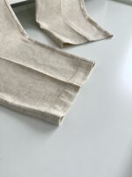 Dettaglio di tessuto beige con orli cuciti a mano, ideale per abbigliamento e accessori artigianali.