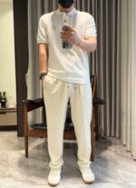 Persona con outfit casual bianco: polo, pantaloni comodi, sneakers e mascherina in ambientazione moderna.