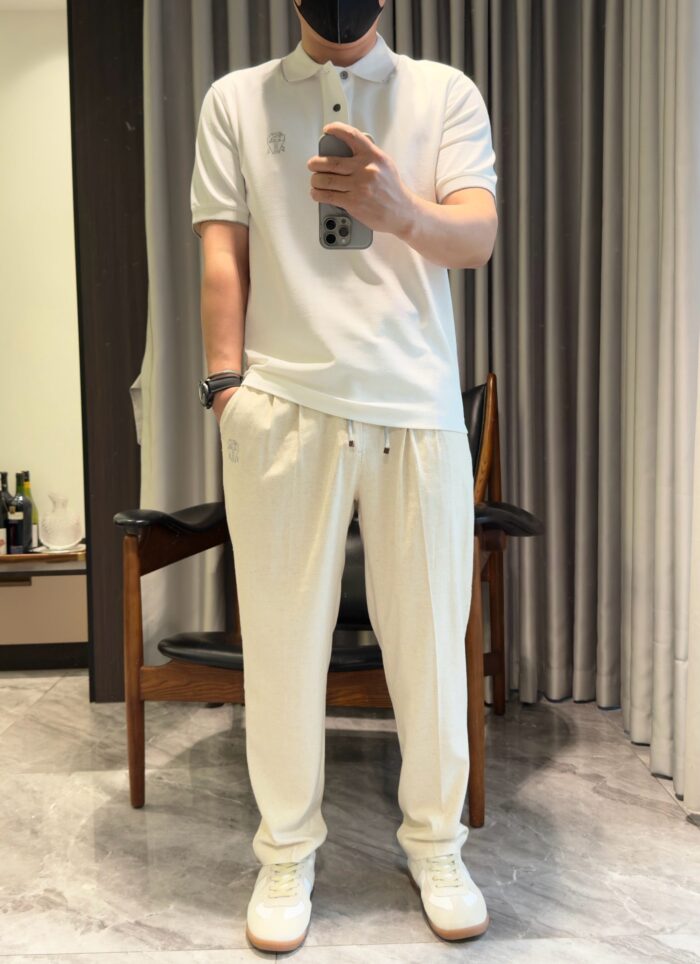Persona con outfit casual bianco: polo, pantaloni comodi, sneakers e mascherina in ambientazione moderna.