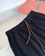 Pantaloni neri casual con cintura elastica e dettagli in marrone, sfondo colorato e vivace.