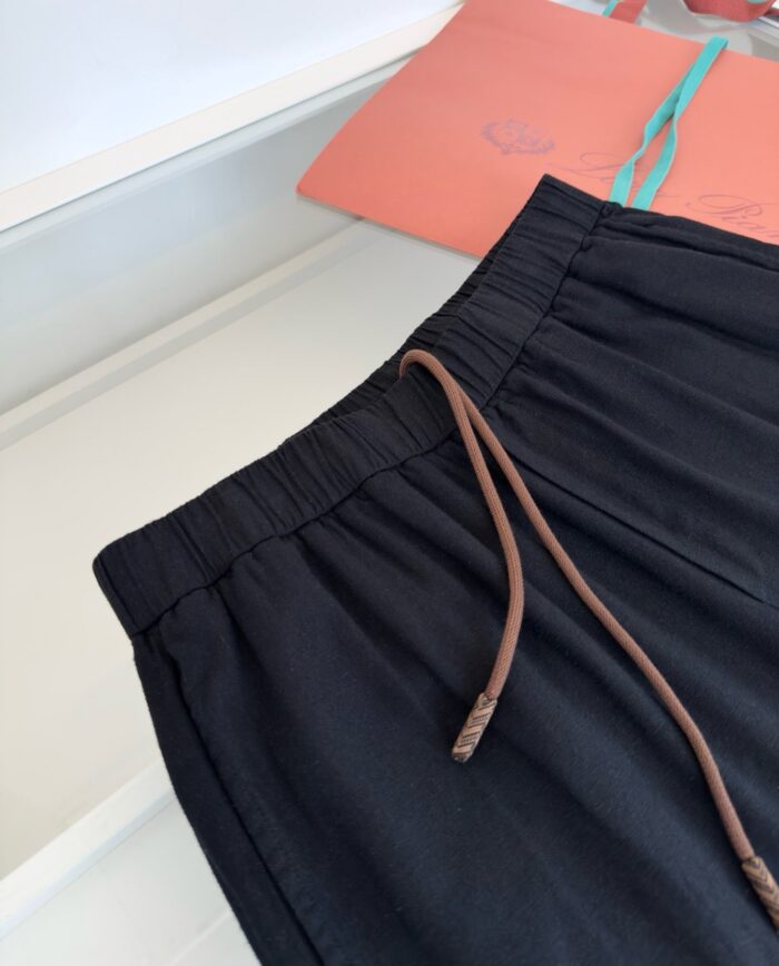 Pantaloni neri casual con cintura elastica e dettagli in marrone, sfondo colorato e vivace.