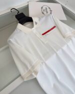 Maglietta polo bianca con dettaglio rosso, logo elegante e design moderno.